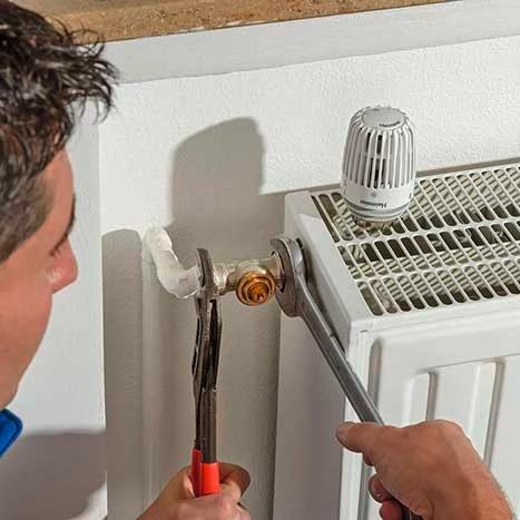 Mann erneuert Ventil und Thermostat an Heizkörper